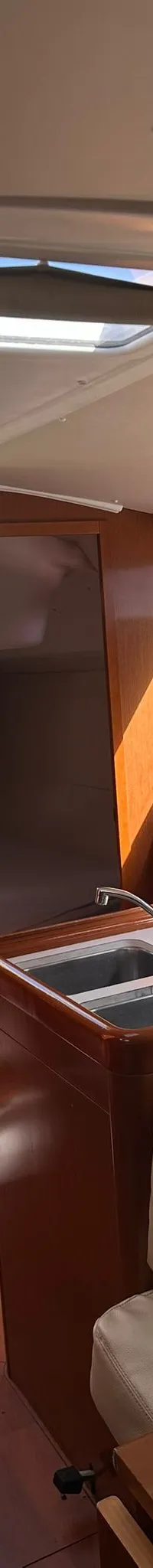 De foto toont het interieur van een boot met een kombuis, zithoek, houten vloer en een trap naar het dek.