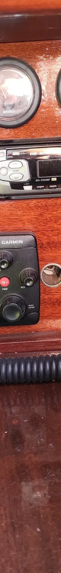 Een houten paneel met schakelaars, meters, een radio, een marifoon met microfoon en een aparte luidspreker is zichtbaar.