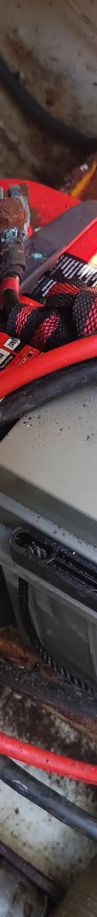 Twee accu's, een rode en een grijze, zijn vastgezet met banden en verbonden met diverse kabels in een bootcompartiment.