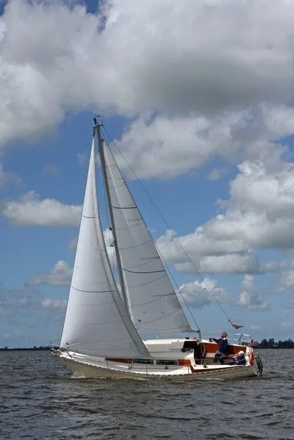 Een witte zeilboot met twee personen aan boord vaart op het water onder een bewolkte blauwe lucht. — Vitessa 860 Motorzeiler