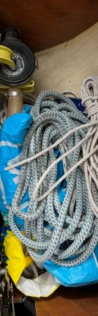 Een opbergruimte met opgerolde touwen, een gele handpomp en blauwe en gele tassen.