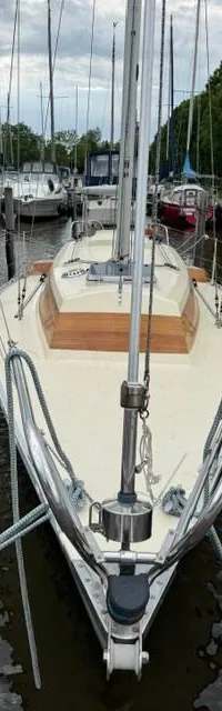 Een zeilboot met crèmekleurig dek en houten accenten ligt afgemeerd in een jachthaven, omringd door andere boten.