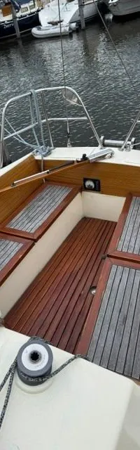 De kuip van een zeilboot met houten banken en vloer is zichtbaar, met een reddingsboei aan de achterreling.