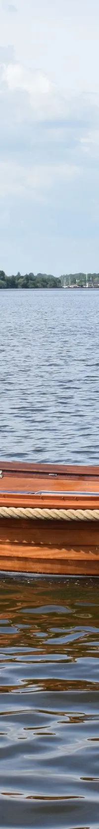 Een houten sloep met een persoon aan het roer vaart over het water, met de naam "Amsterdam" op de spiegel.