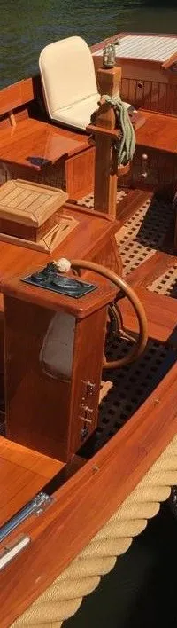 Een houten boot met een stuurwiel, beige kussens en een gevlochten stootrand ligt aangemeerd aan een houten steiger.
