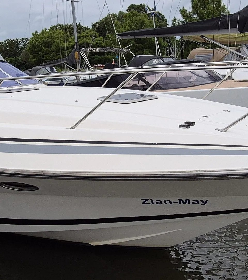 Een witte motorboot met de naam "Zian-May" ligt in het water, met een anker en stootwillen zichtbaar.