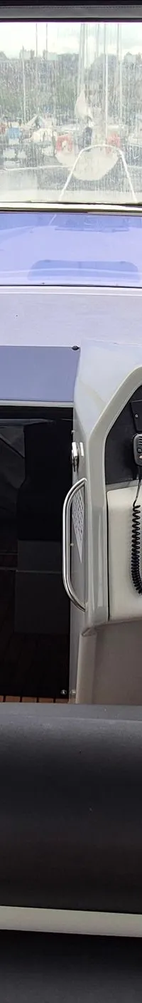 De foto toont de cockpit van een boot met een stuur, instrumentenpaneel, zwarte gestoffeerde banken en een houten vloer.