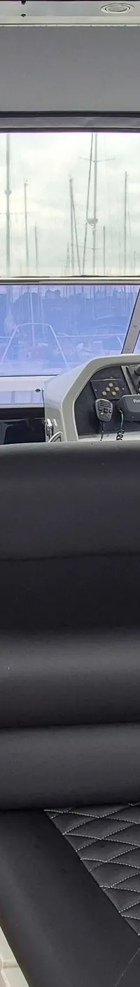 De foto toont het interieur van een boot met een stuurstand, zwarte gestoffeerde zitbanken en een houten vloer.