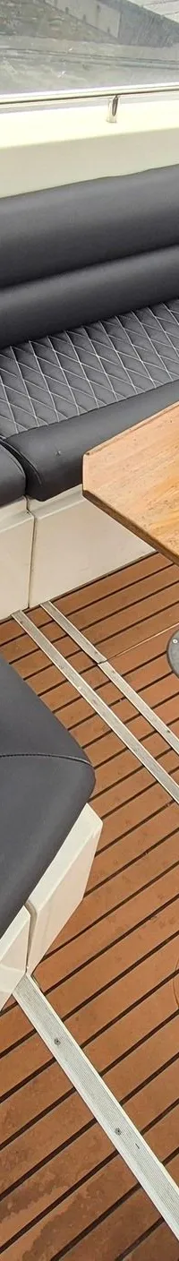 De foto toont een bootinterieur met een U-vormige zwarte bank, een houten tafel en een houten vloer.