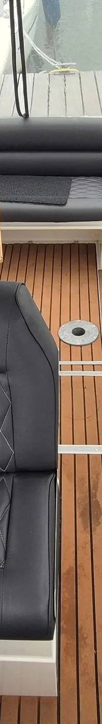 De foto toont het interieur van een boot met een U-vormige zwarte bank, een houten tafel en een houten vloer.
