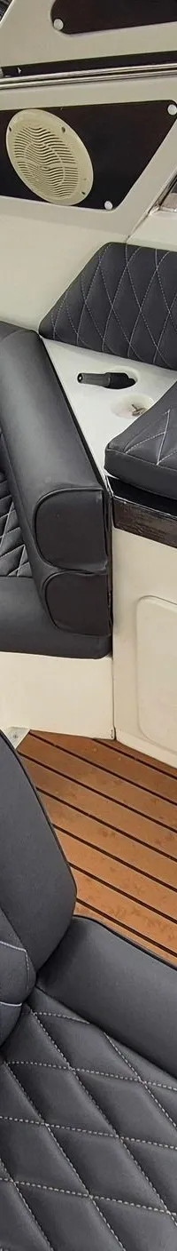 De foto toont een bootinterieur met een U-vormige zwarte bank, een houten tafel en een teakhouten vloer.