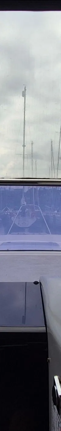Een interieurfoto van een boot met een stuurconsole, een Raymarine marifoon en een voorruit met uitzicht op zeilboten in…