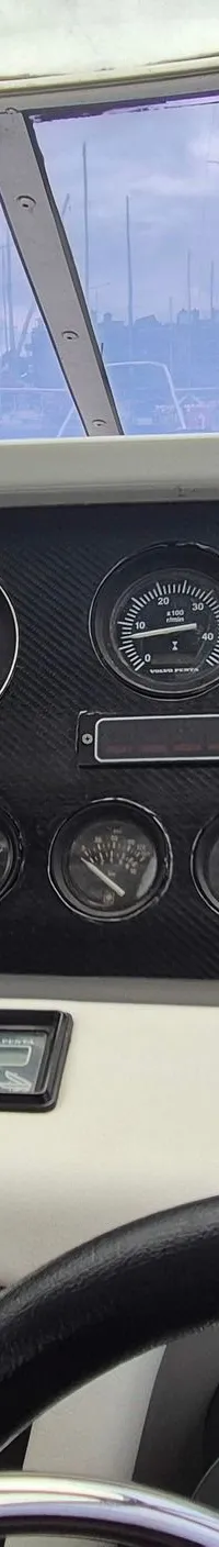 Een stuurstand met een stuurwiel, diverse meters, een Raymarine marifoon, een Lowrance dieptemeter en een uitzicht op een…