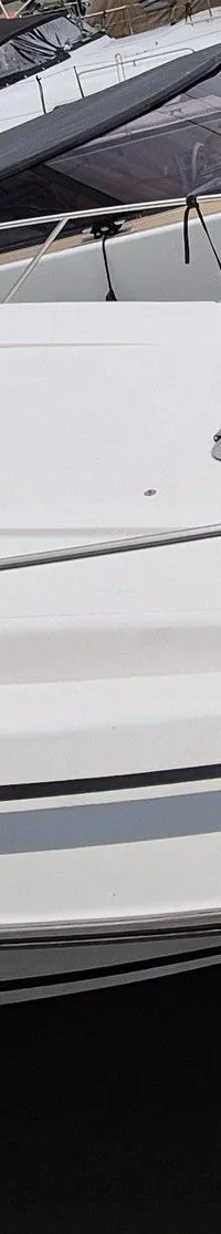 Een witte motorboot met een zwarte kap en blauwe ramen ligt in het water, met andere boten op de achtergrond.