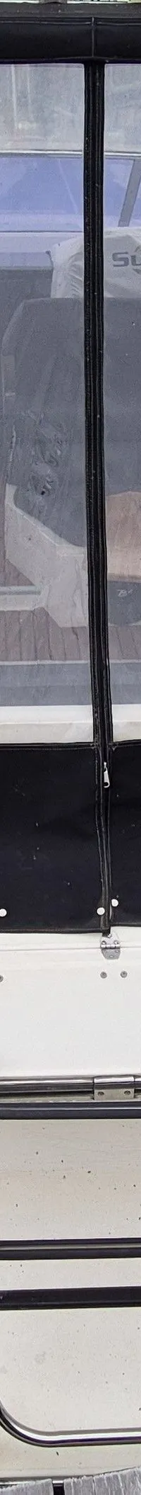 Een witte boot met een zwarte kap en doorzichtig plastic zeil ligt aangemeerd aan een houten steiger.