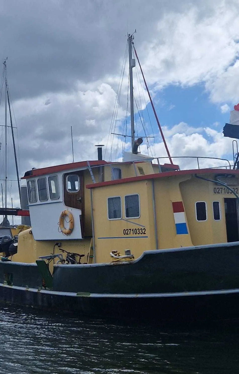 Een geel-zwart schip met een Nederlandse vlag aan de achtersteven, afgemeerd in een haven.
