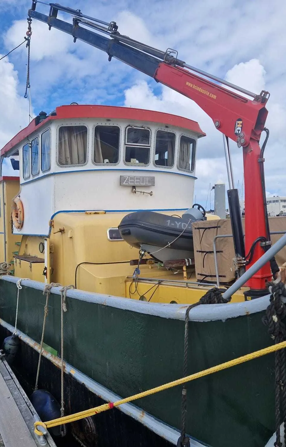 Een geel-groene boot met de naam "ZEEUL" ligt afgemeerd aan een houten steiger, met een rode kraan op het dek.