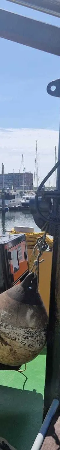 Een oranje Daewoo noodgenerator hangt aan een kraan boven een groen dek, met een jachthaven op de achtergrond.