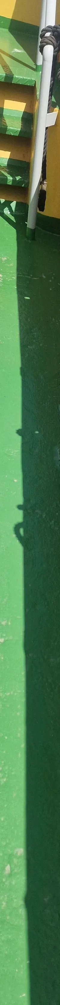 Een groen dek met gele zijkanten en een trap, met een kraan en touwen, en een schaduw van een persoon.