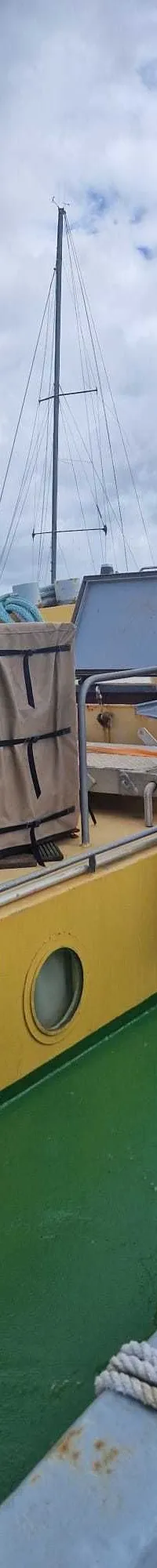 Een dek van een boot met een rubberboot, een rode kraan, patrijspoorten en zeilboten op de achtergrond.