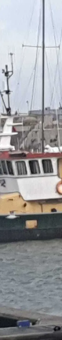 Een groene, gele en witte boot met een rood-wit gestreepte boeg ligt afgemeerd in een haven.
