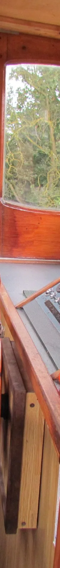 Een interieur van een stuurhut met houten wanden, een blauwe stoel, een houten stuurwiel en diverse bedieningselementen.