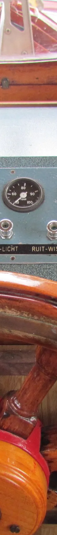 Een houten stuurwiel met een bedieningspaneel met meters en schakelaars is zichtbaar.