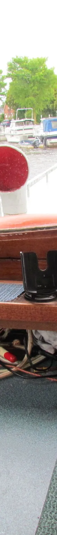 De foto toont het interieur van een stuurhuis met houten kozijnen en een uitzicht op een kanaal met aangemeerde boten.
