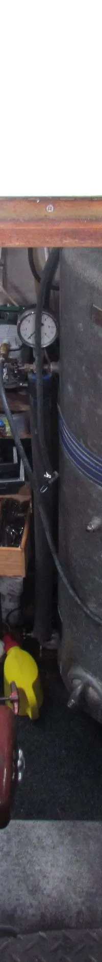 Een blik in de motorruimte van een boot, met een roodbruine motor en een grote grijze tank.