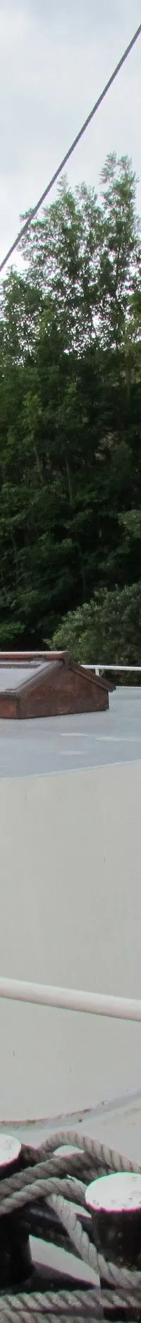 Een witte boot met rode en zwarte accenten ligt aangemeerd aan een kade, met een houten mast en stuurhut.