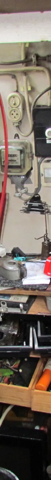 Een rommelige machinekamer met een grote grijze tank, diverse meters, kabels, gereedschap en een brandblusser.