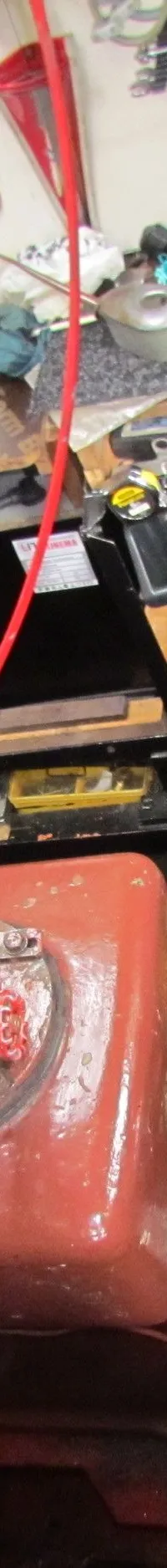 Een roodbruine motor met een rood vliegwiel, omringd door diverse apparatuur en een grote grijze tank.