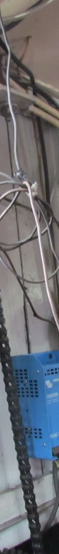 De foto toont een interieur met een wirwar van leidingen, kabels, een stopcontact, een blauwe omvormer en een motoronderdeel.
