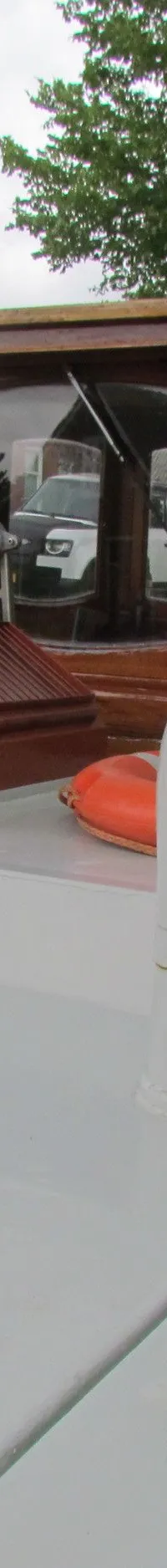 Een bovenaanzicht van het dek van een boot met een houten stuurhut, reddingsboeien en een zonnepaneel.
