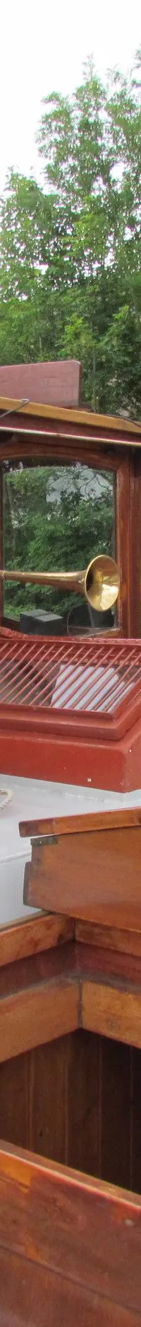 Een houten stuurhut met ramen en een scheepshoorn, twee oranje reddingsboeien en een open luik op het dek.