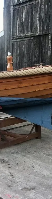 Een houten boot met de naam "HEEG" op de spiegel, staat op een trailer voor een houten schuur. — De Jong Vlet 6.20