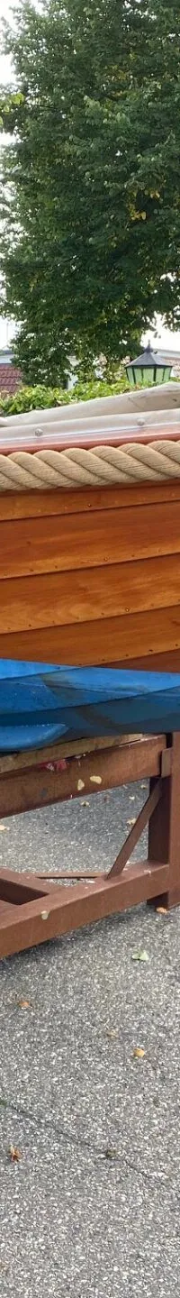 Een houten boot met een blauwe onderkant staat op een bruine bok op een geasfalteerde ondergrond. — De Jong Vlet 6.20
