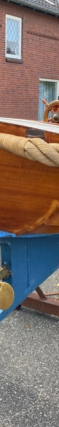Een houten boot met een blauwe onderkant en een gouden schroef staat op een bruine bok op een geasfalteerde ondergrond.