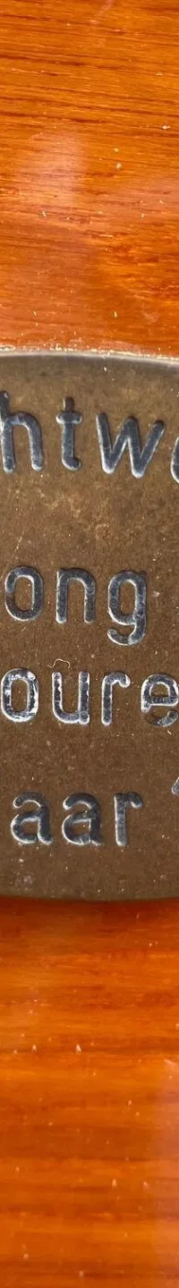 Een ovale, bronzen plaat met de tekst "Jachtwerf De Jong b.v. Joure Bouwjaar 1985" is vastgeschroefd op een houten oppervlak.