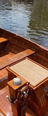 Een houten boot met een stuurwiel, kompas en een touw langs de rand, drijvend in het water. — De Jongvlet 6.20
