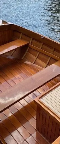 Een houten boot met een touw langs de rand ligt aan een houten steiger, met glanzende houten banken en vloer.