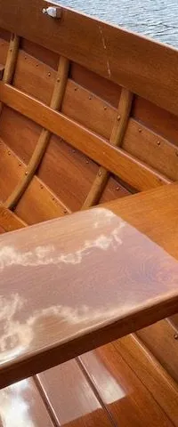 De foto toont het interieur van een houten boot met banken en een glanzende afwerking, met de weerspiegeling van wolken op…