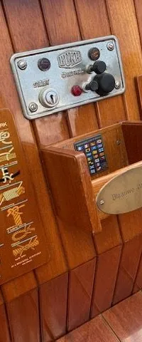 Een detailfoto van een houten bootinterieur met een bedieningspaneel, knopenkaart en vlaggenkaart.