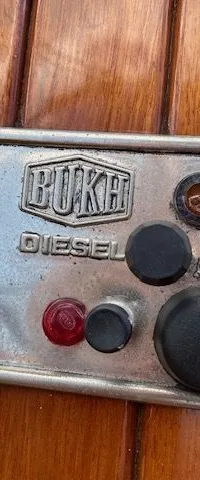 Een zilverkleurig bedieningspaneel met "BUKH DIESEL", "START" en "STOP" knoppen, gemonteerd op een houten oppervlak.