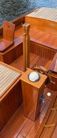 Een houten boot met een stuurwiel, twee stoelen met hartvormige uitsparingen en een tafel, ligt afgemeerd aan een steiger.
