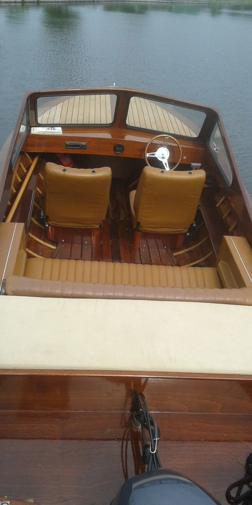 Een houten boot met bruine bekleding en een stuurwiel, liggend in het water. — Flying Finn 19.60