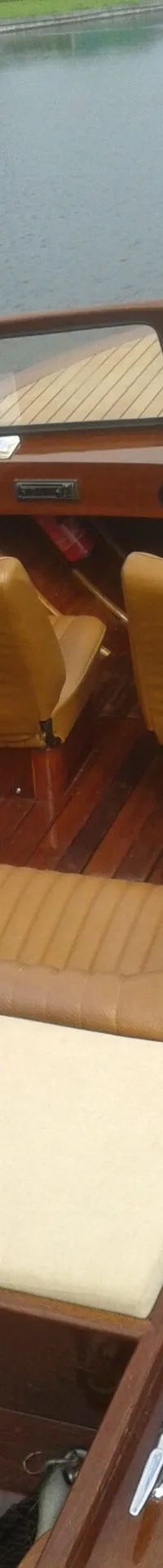 Een houten motorboot met bruine bekleding en een stuurwiel ligt in het water. — Flying Finn 19.60