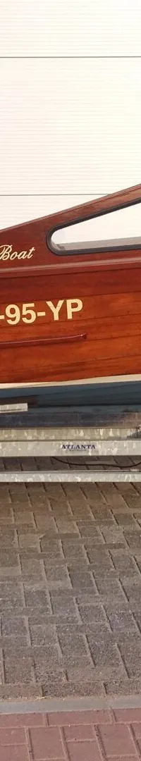 Een houten boot met de naam "The Boat" en registratienummer "96-95-YP" staat op een trailer met een Yamaha buitenboordmotor.