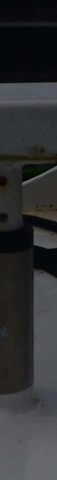 Een wit dek met een witte, metalen beugel, een opgerold zwart touw en een houten rand.