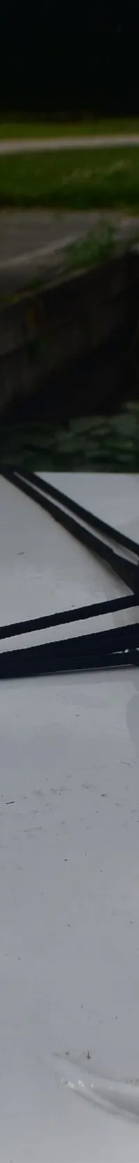 Een deel van een wit bootdek met een vlag, touwen, een metalen paal en een donkerblauwe kap.